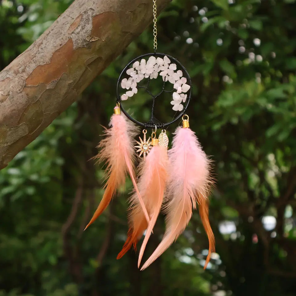 Pink crystal Tree of Life feather hanging displayed near a tree